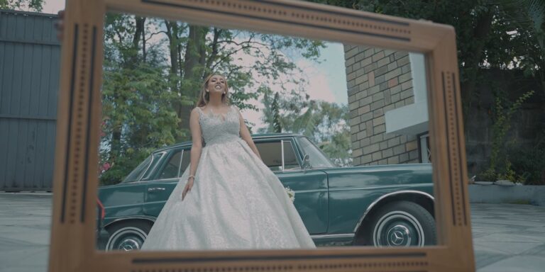 Bride in a wedding gown beside a vintage car, photographed by Gift Habeshaw
